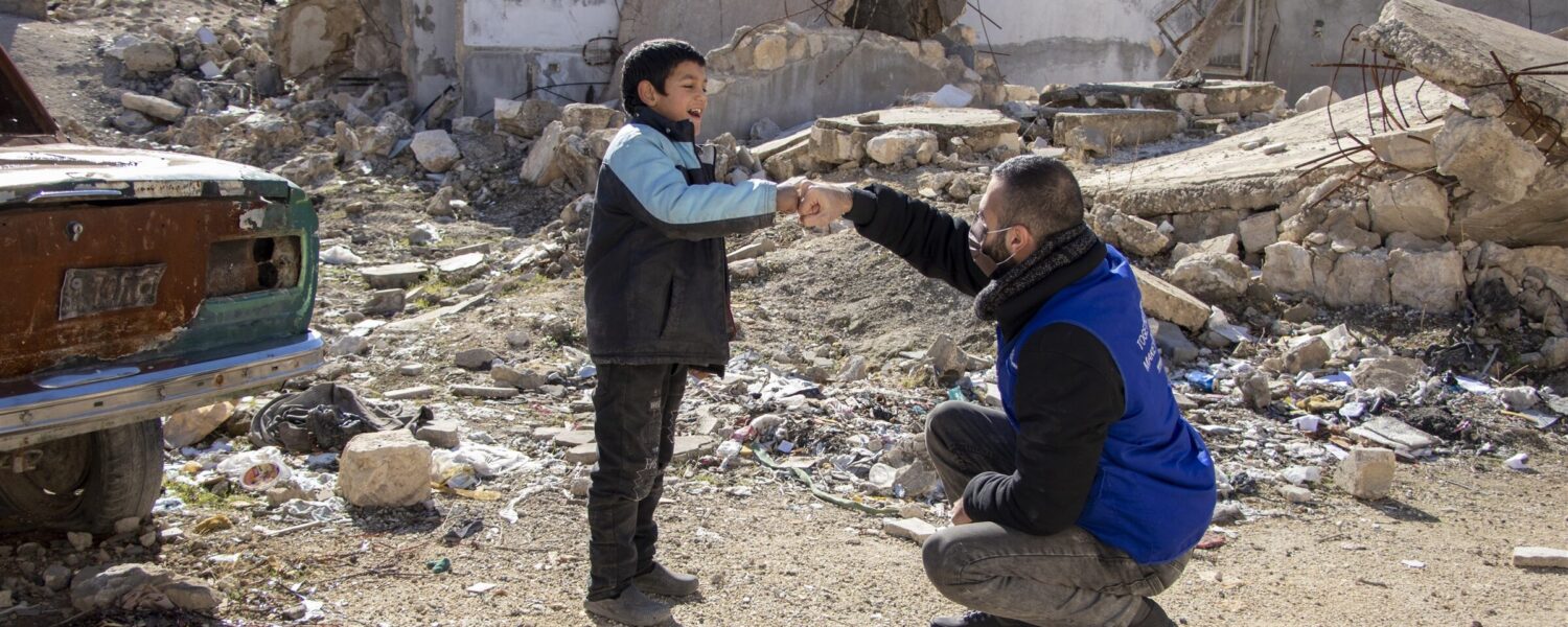 Dorcas-medewerker met kind voor een kapot gebouw in Libanon
