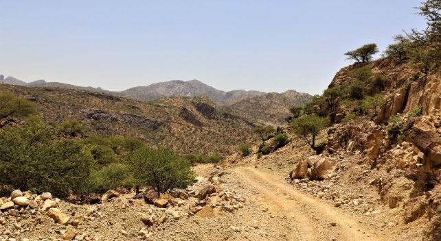 Rustige stoffige weg door een bergachtige, droge landschap met sparse begroeiing en rotsformaties in een semi-aride omgeving.