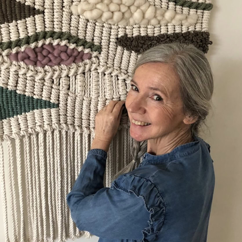 Kunstwerk van gehaakte muurdecoratie door Dorcas met een lachende vrouw die de textuur en details van het handgemaakte wandkunstwerk toont.