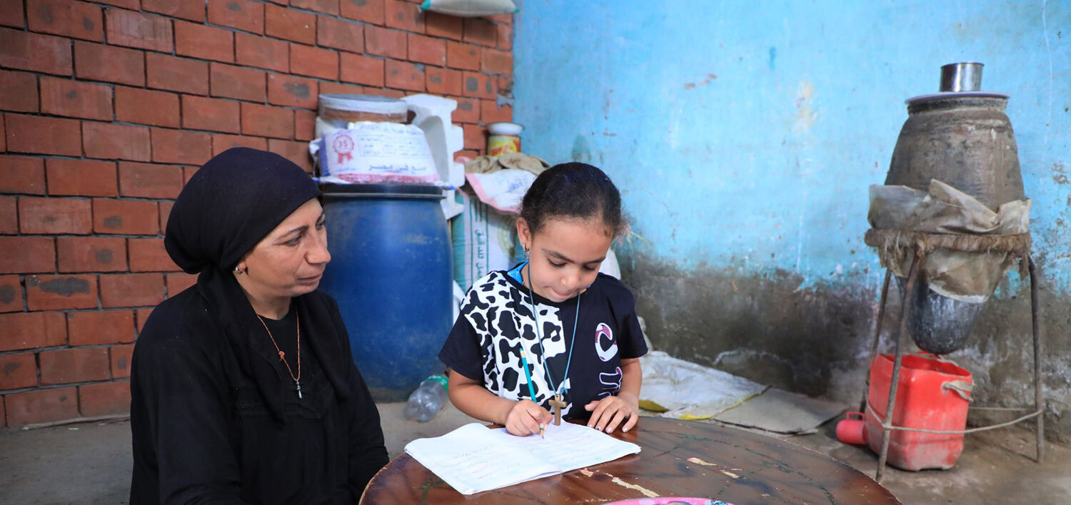 Kind vrouw en meisje leren samen in een eenvoudige kamer met bakstenen muur en schoorsteen in een ontwikkelingsland.