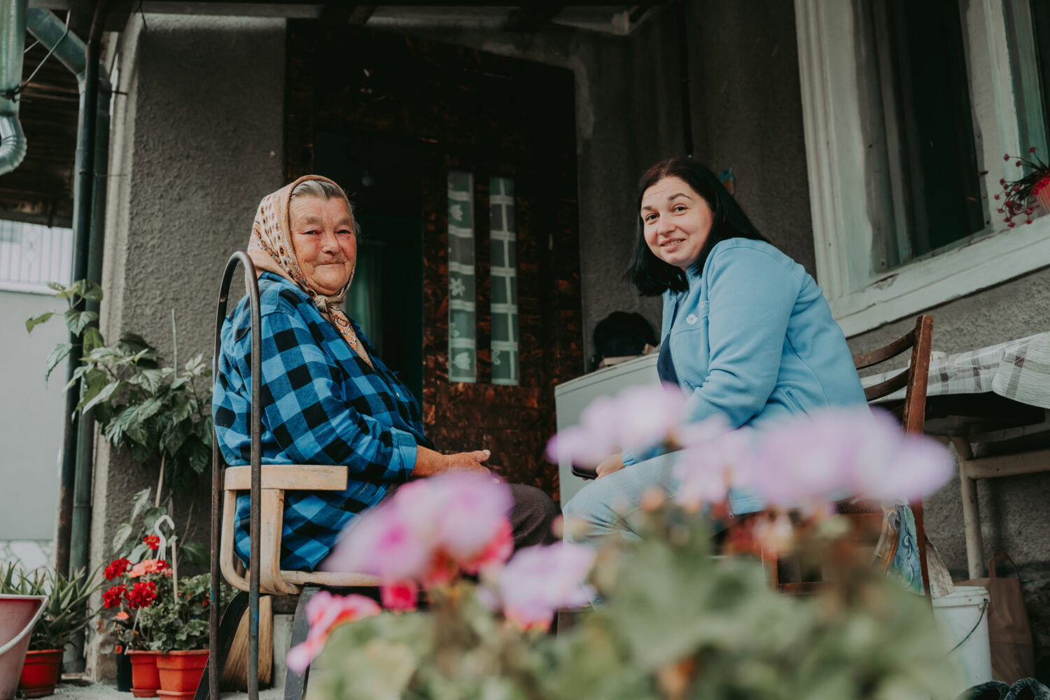 Oudere vrouw krijgt bezoek van jonge vrouw op haar veranda, samen lachen en praten.