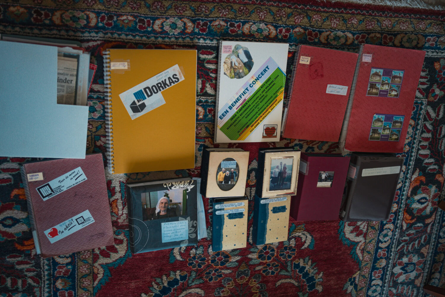 Gepersonaliseerde fotoboeken en herinneringen op een kleurrijk vloerkleed, inclusief collecties van Dorcas en herinneringsalbums met familie foto’s.