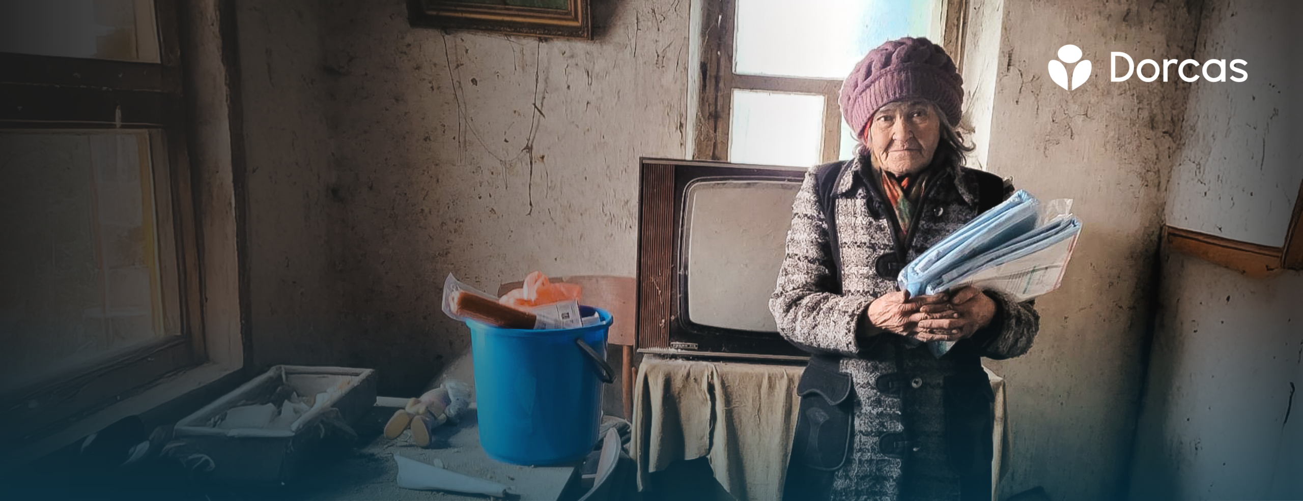 Een vrouw in een armzalige kamer ontvangt hulp en houdt documenten vast, symboliseert de noodhulp voor Oekraïne en de inzet van Dorcas voor humanitaire ondersteuning.